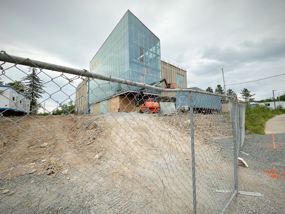 Access is blocked by a closed chain-link fence in front of a new building with tall glass windows surrounded by dirt.