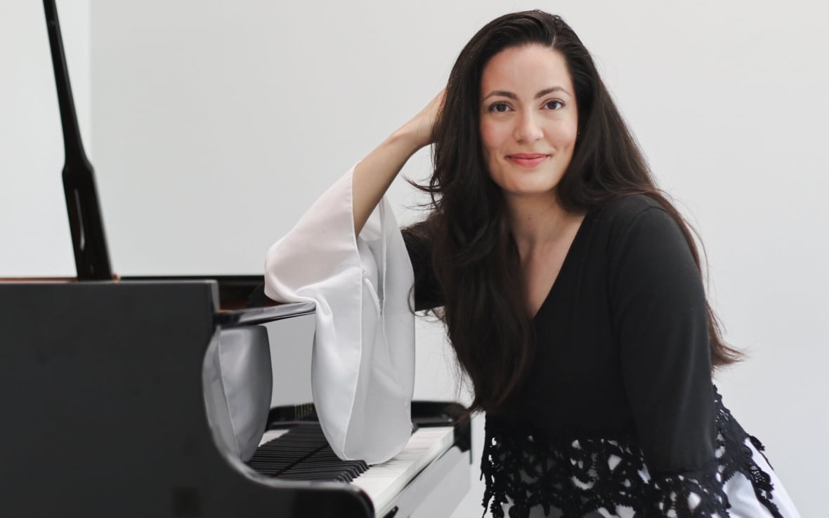 Elisabeta Cojocaru is pictured seated at a black grand piano in a white room.