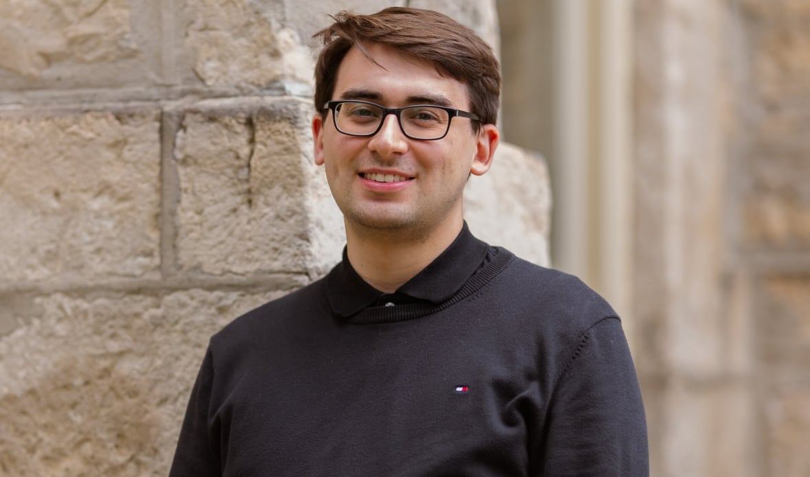 Composer Justin Lapierre poses in front of a stone wall.