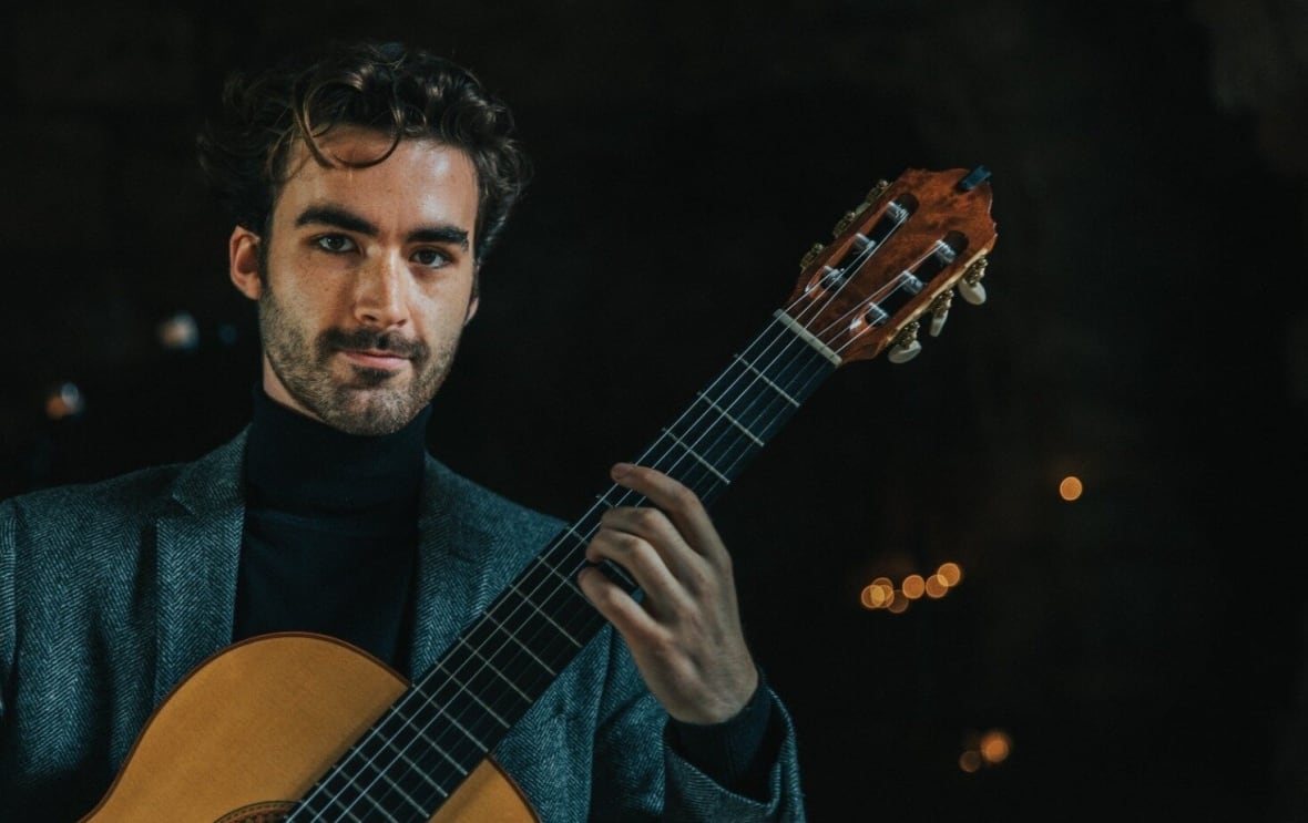 Tim Beattie poses with his classical guitar against a black backdrop.