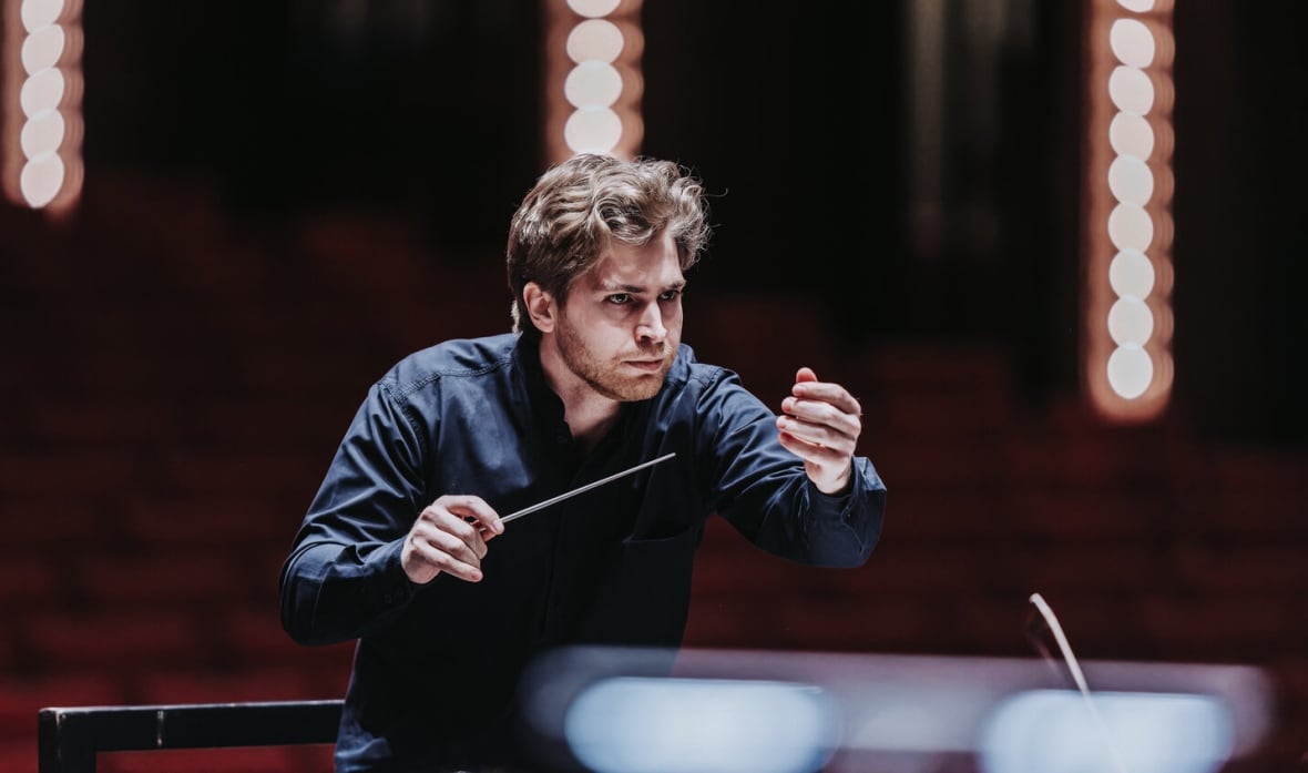 Conductor Henry Kennedy leads an orchestra with a baton in his hand.
