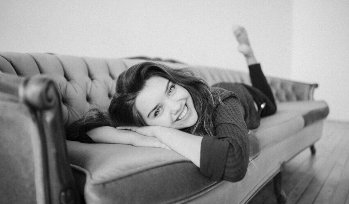 Mezzo-soprano Kady Evanyshyn lies on a sofa and smiles for the camera.