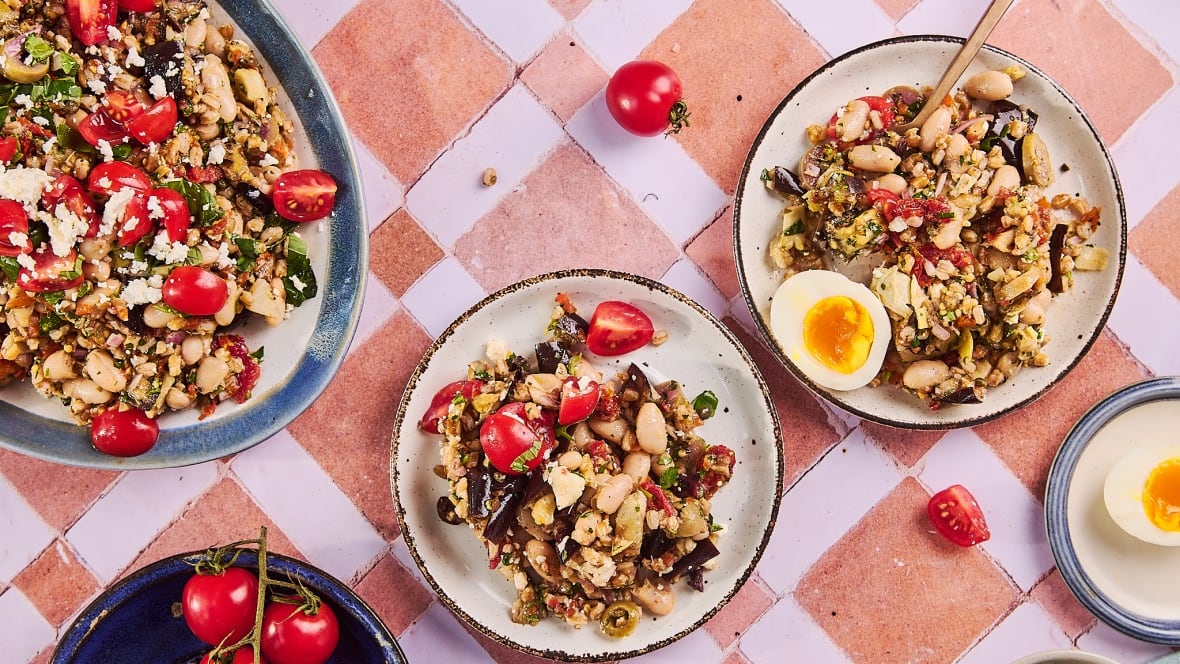 Top down shot of a platter and two plates filled with farro and white bean salad topped with tomatoes.