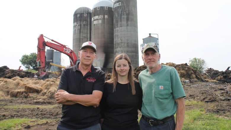 Two men and a woman pose in front of the site where their family's barn stood