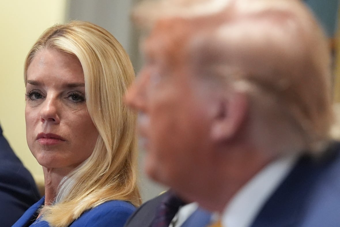 A blonde haired woman is shown in focus, while to her left an older man is shown blurred.