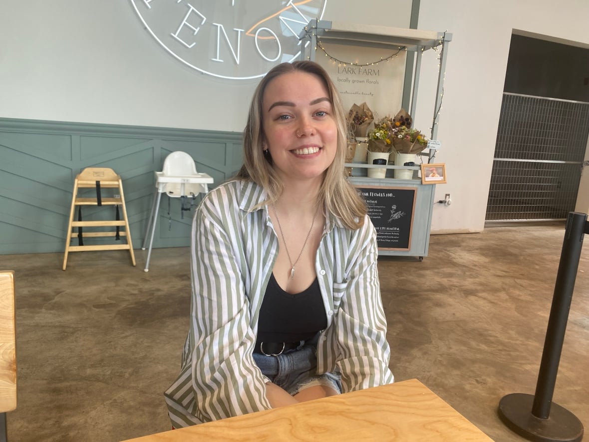 A smiling blonde woman sits at a table of a coffee shop.