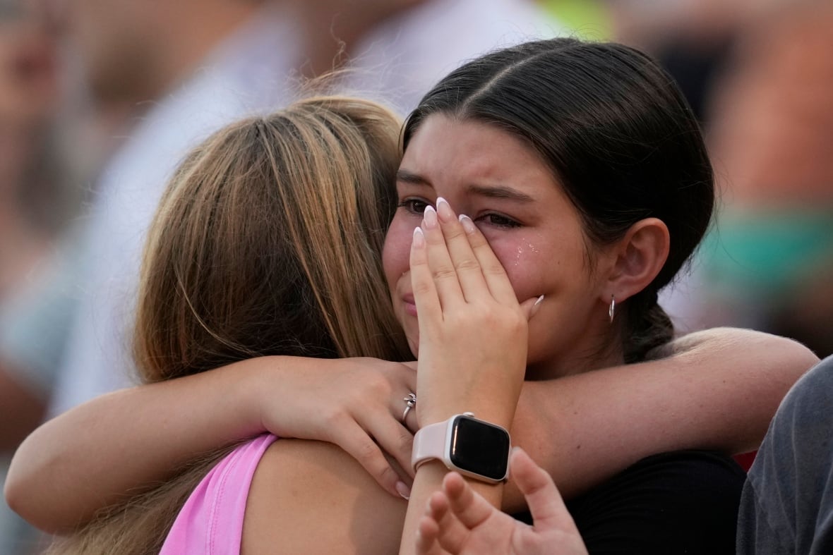 A young girl wipes her eyes while in an embrace with another female with their back to the camera.