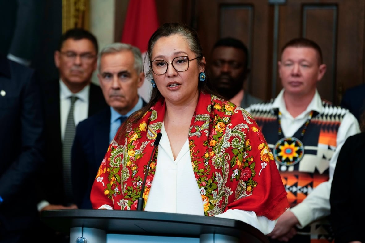 A woman speaks as a podium as others listen on in the background outside the House of Commons.