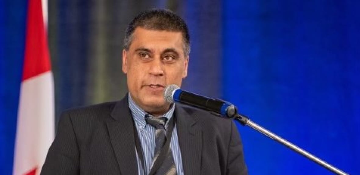 Man in a black suit stands in a podium, in front of a microphone