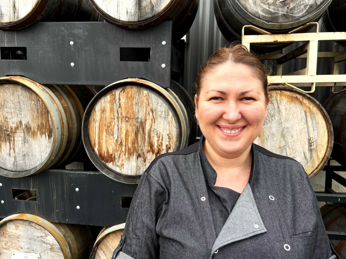 A woman stands in front of a wall of barrels.