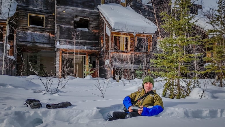 Explorer Felipe Gomez lies in the snow in front of abandoned housing complex in Uranium City, Saskatchewan.