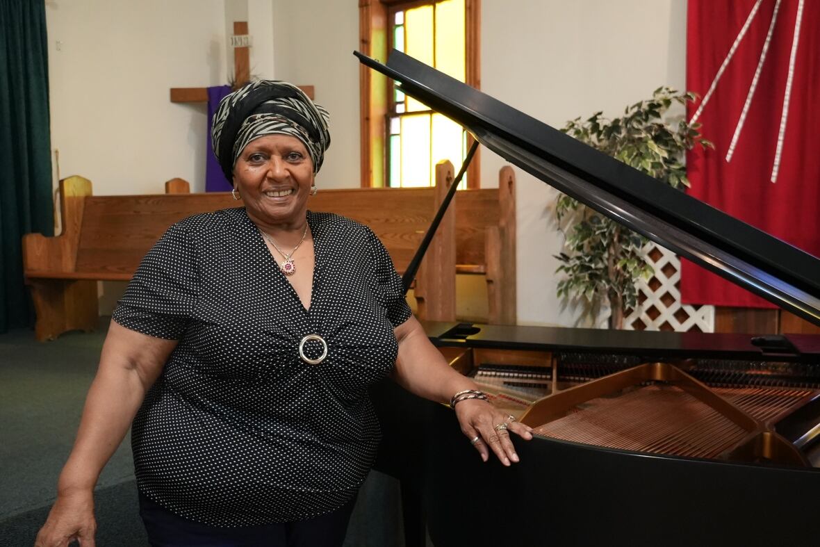 A woman in a black shirt stands in front of a piano in a church.