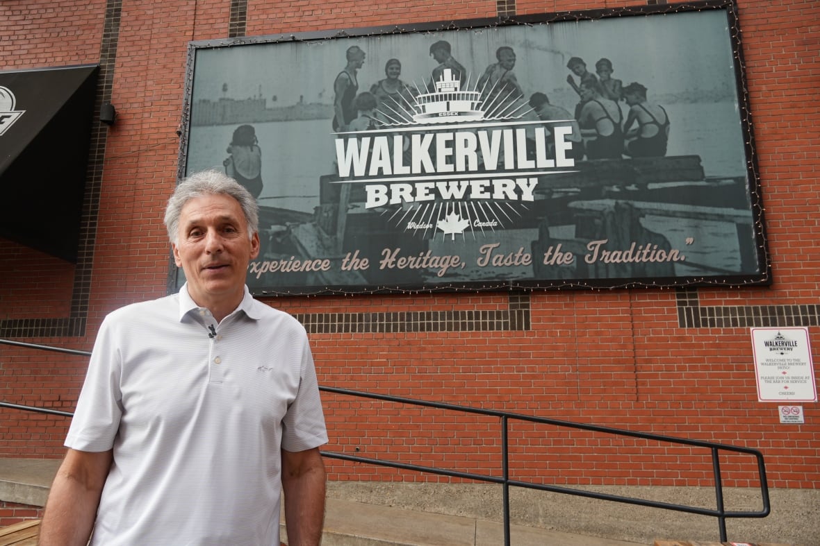 A man in a grey golf shirt stands in front of a brick building and a sign that reads "Walkerville Brewery"