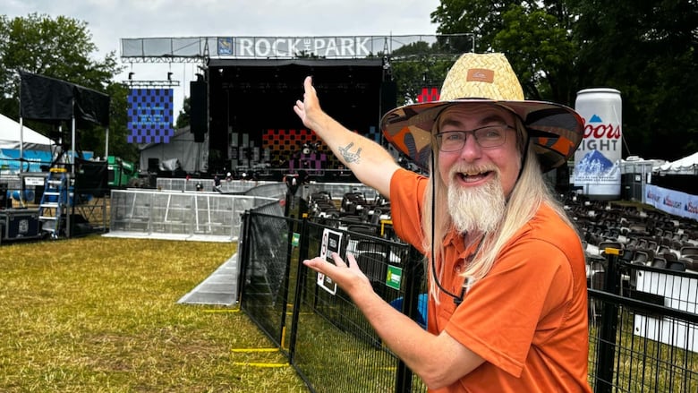 A man points at a stage with a "Rock the Park" banner