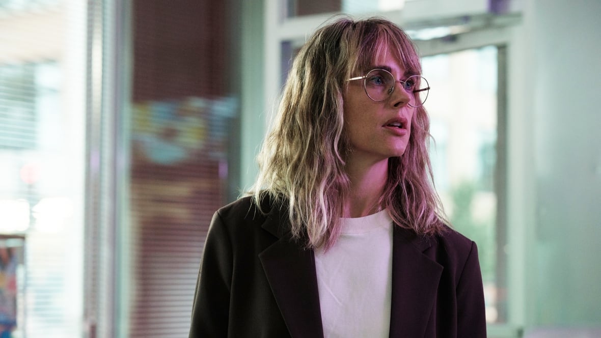 A young woman wearing glasses in dressed in business clothing and looking ahead.