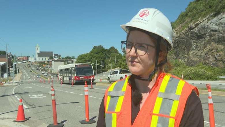 Woman, wearing hard hat and orange construction vest, looking at camera with a neutral expression.