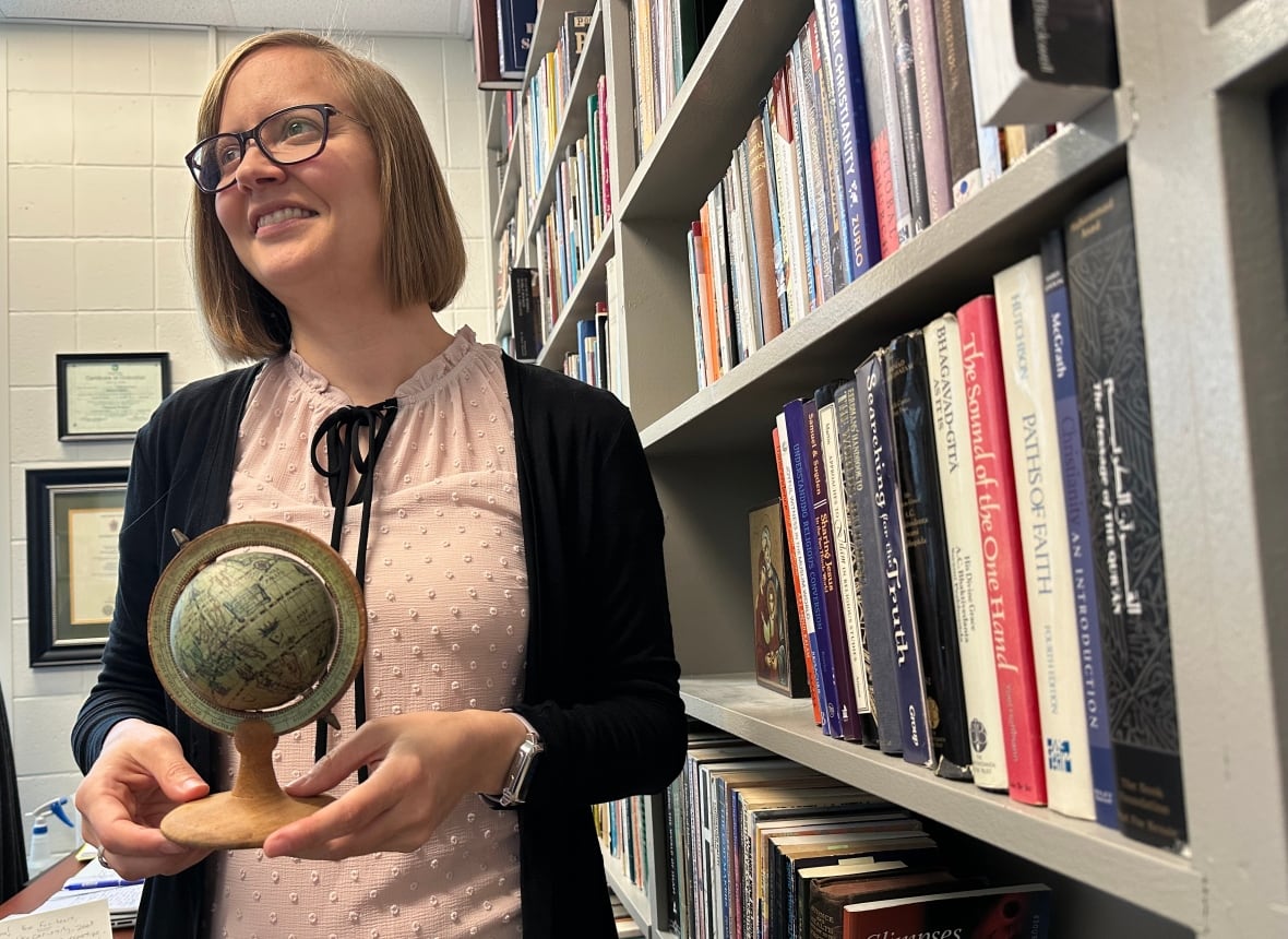 A woman holding a small globe is shown by a bookcase.