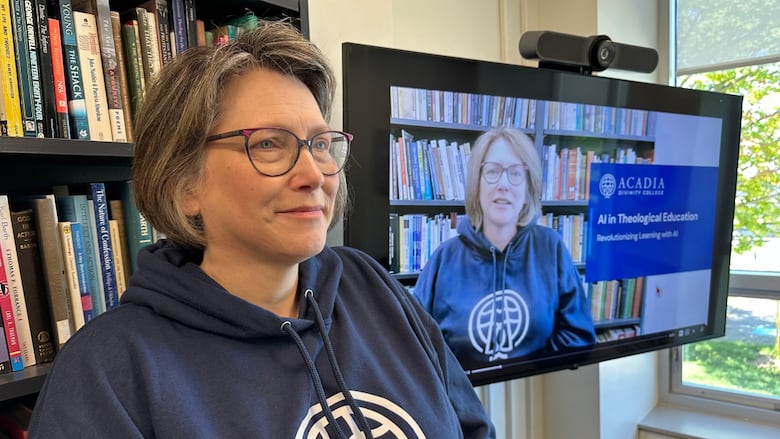 A woman in a blue sweatshirt is next to a screen showing an AI-generated avatar that looks like her.