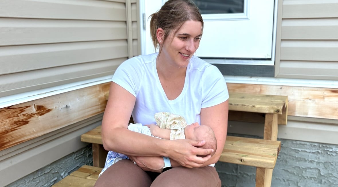 A woman sits in the backyard on a summer day and a baby in her arms.