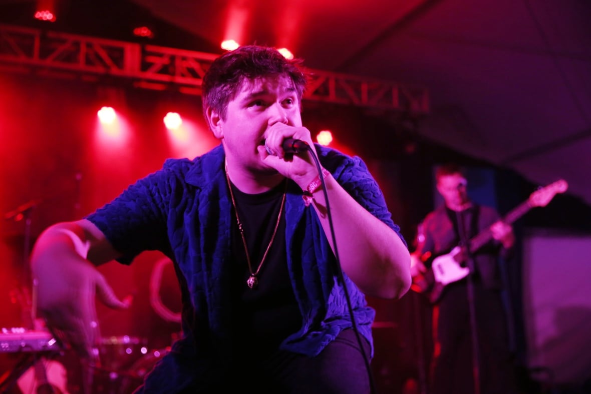A rapper in a blue shirt holding a microphone to his mouth and crouching while performing.