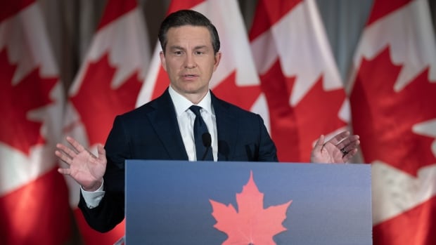A man speaks at a podium in front of Canadian flags.