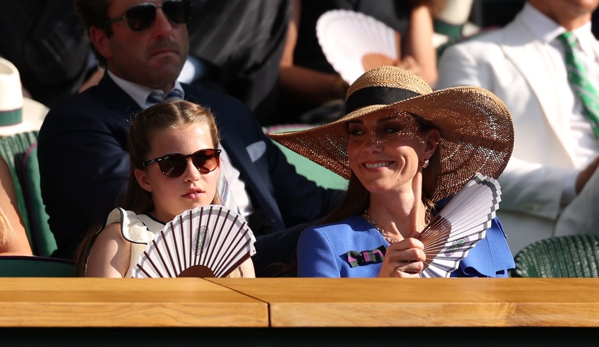 A woman and her daughter hold fans as they watch tennis in a crowd.