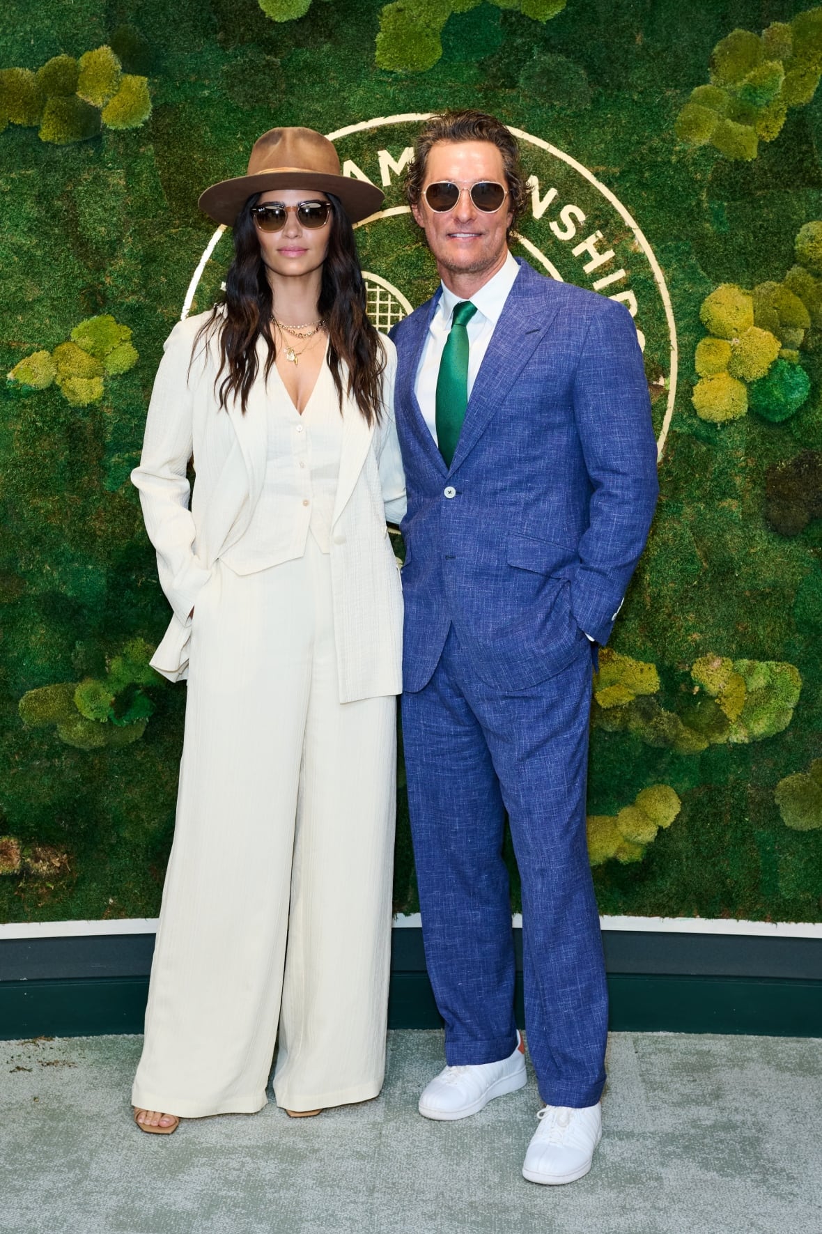 A man and a woman pose for a photo. He's wearing a blue suit and she's wearing a white suit.