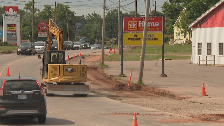 A yellow construction vehicle works while traffic is down to one lane on a main street