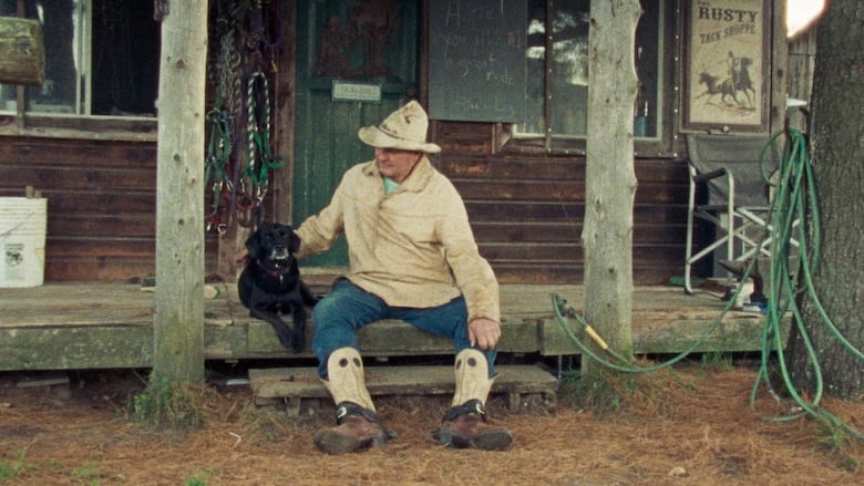A cowboy sits with his dog on a porch.