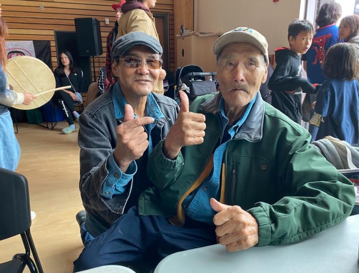 Two older gentleman sit together and both give thumbs up.