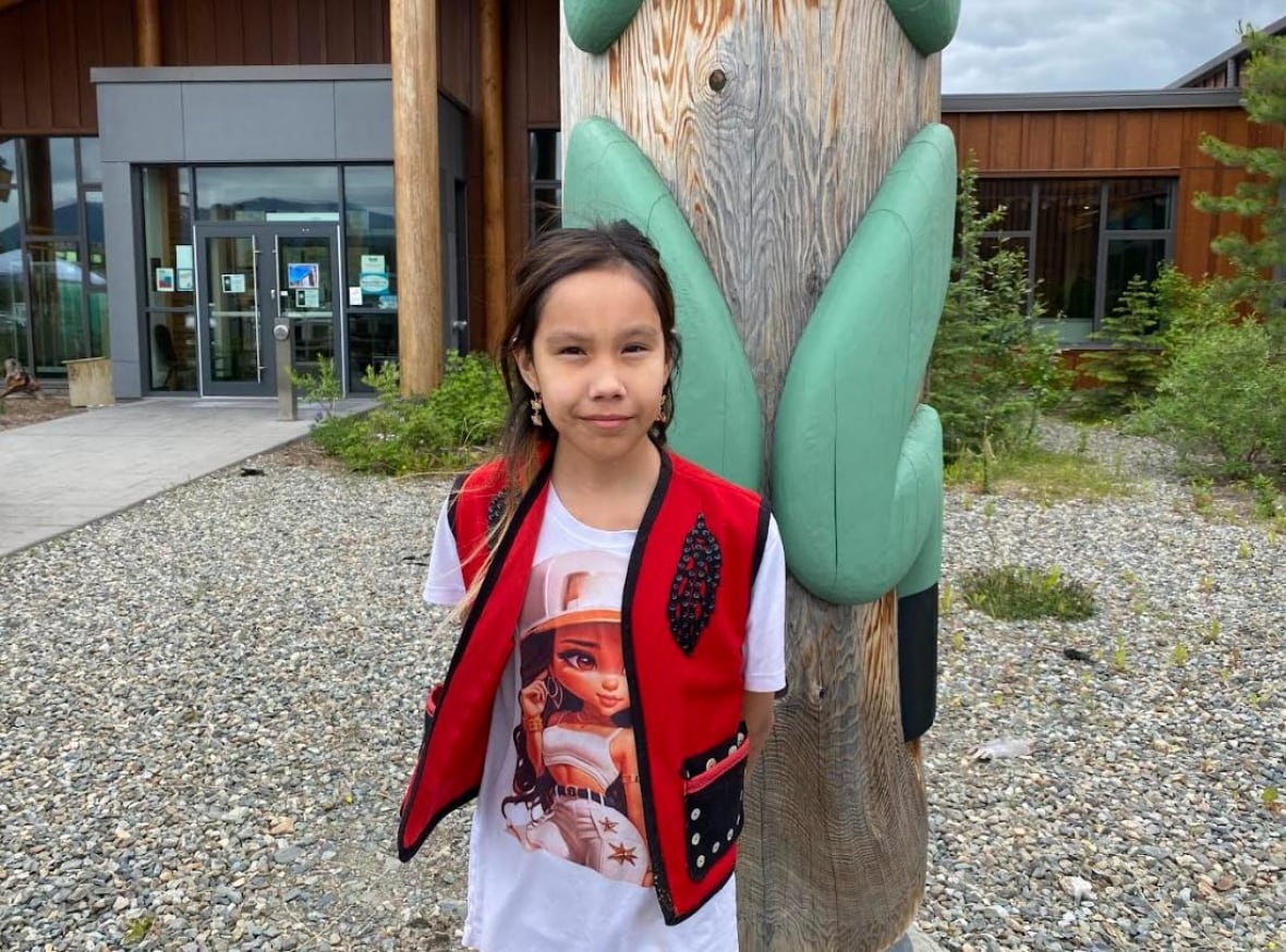 Young girl in red traditional vest stands outside.