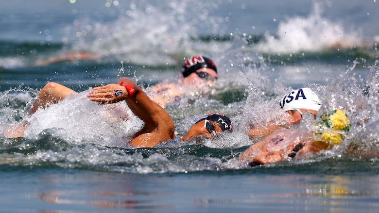 Three swimmers are shown in action in an outdoor body of water.