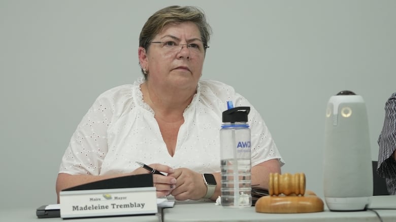 A woman with glasses sits at a table with a gavel 