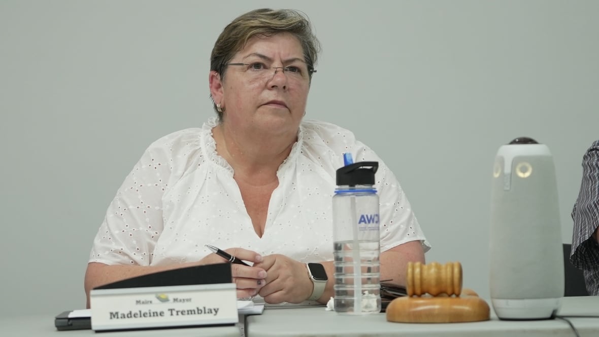 A woman with glasses sits at a table with a gavel 