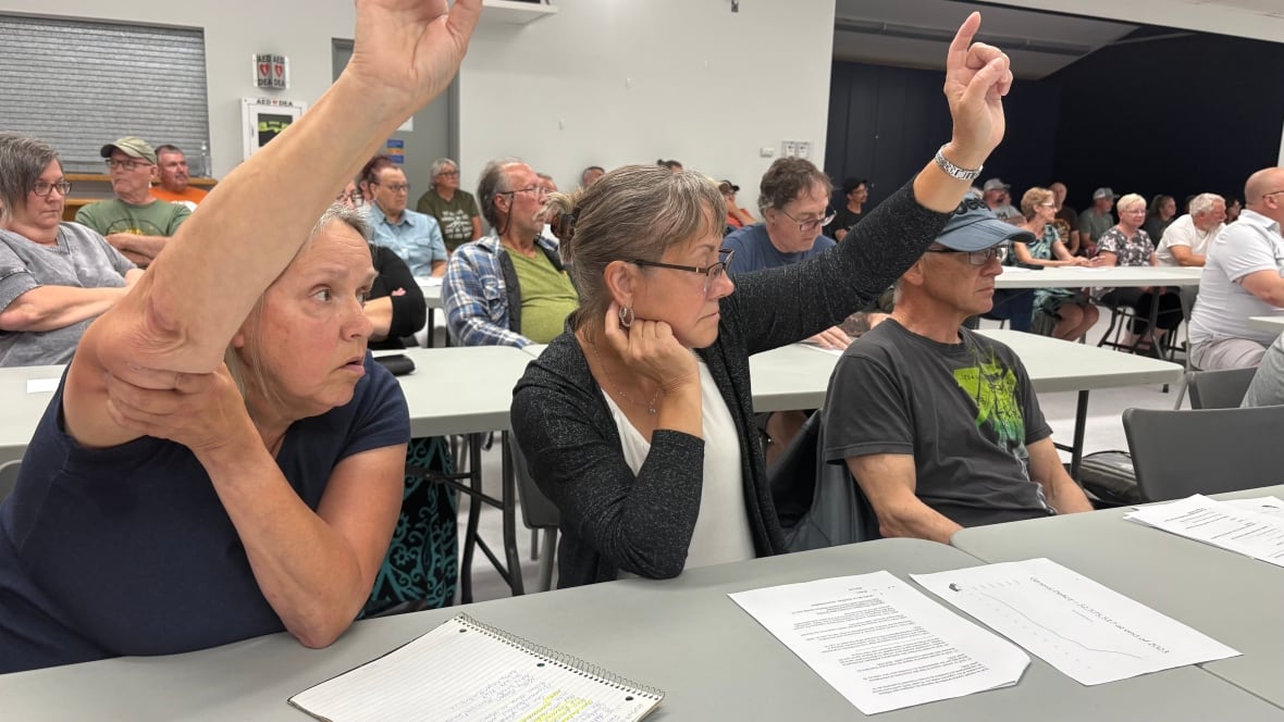 Two people raise their hands in a room full of people