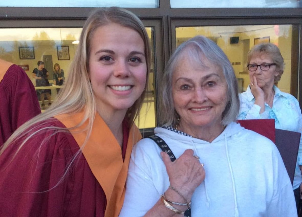 A woman with a red graduation gown and a woman with grey hair and white shirt smiling.