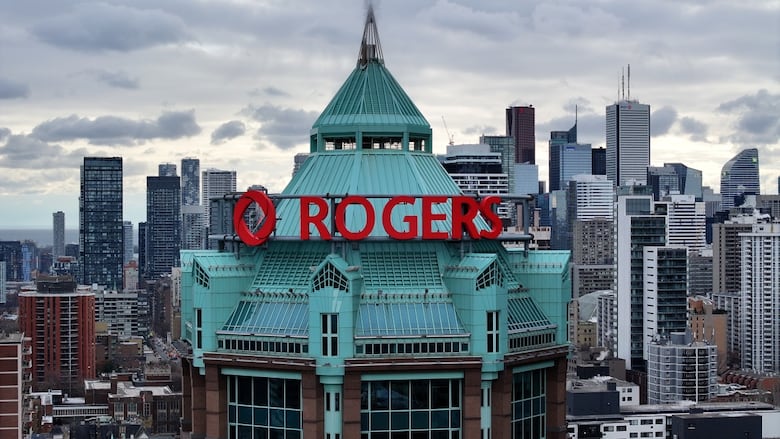 Red brick building with green roof in city landscape, with "Rogers" written across in bright red letters