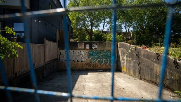 A blue metal fence blocks off a concrete driveway with graffiti on it.
