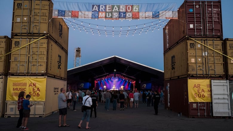 Shipping containers and people in front of a stage with lights and artists on it. 