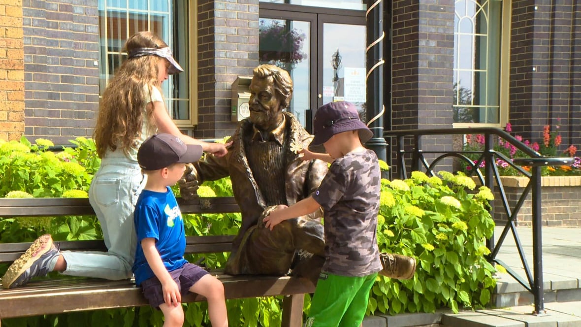 Three children play on a bronze statue of a man sitting on a bench