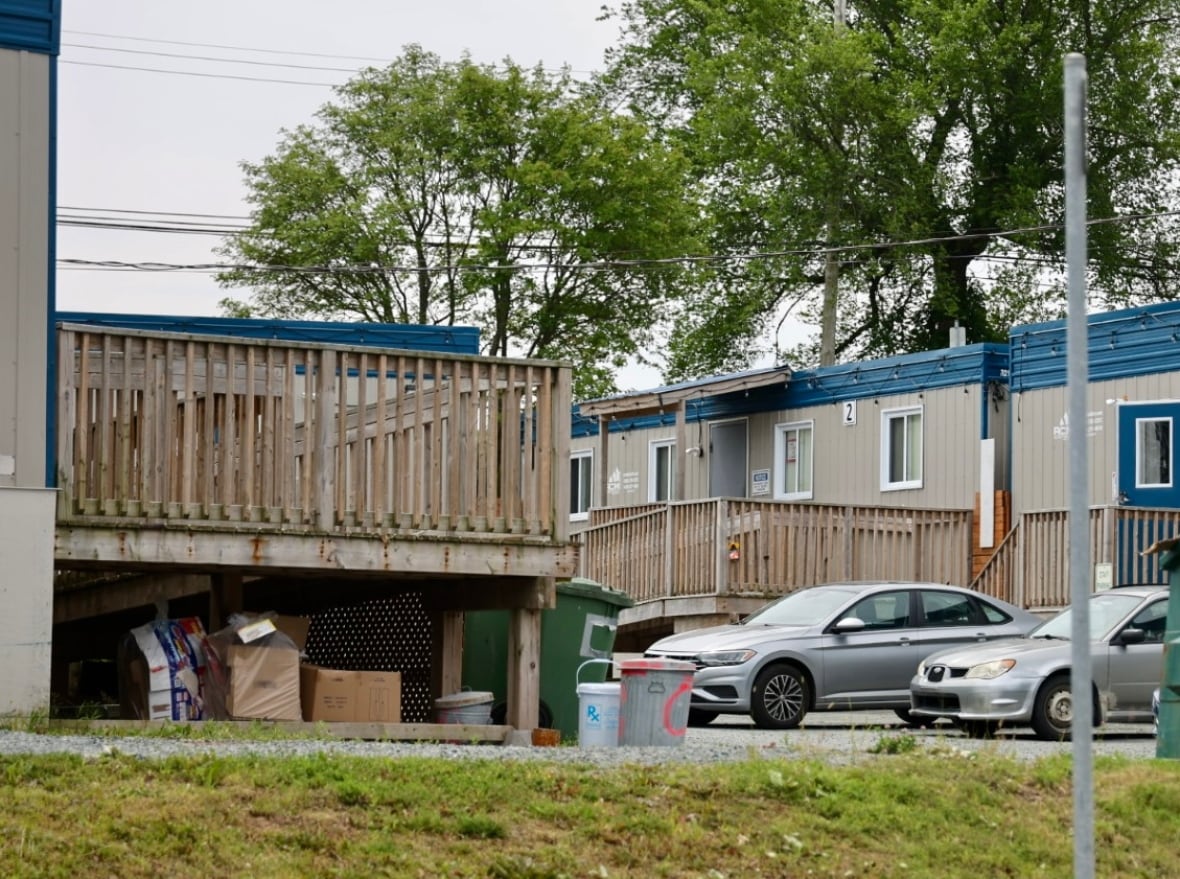 Trailers with wooden ramps, surround by some parked cars, garbage bins and compost bins.