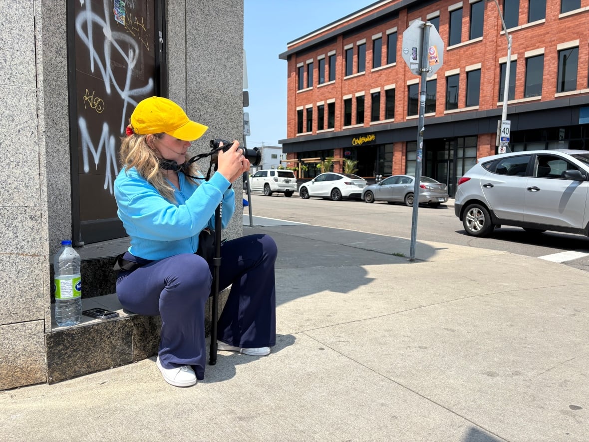 A woman holding a camera on a monopod. She's sitting on a step looking through the lens.