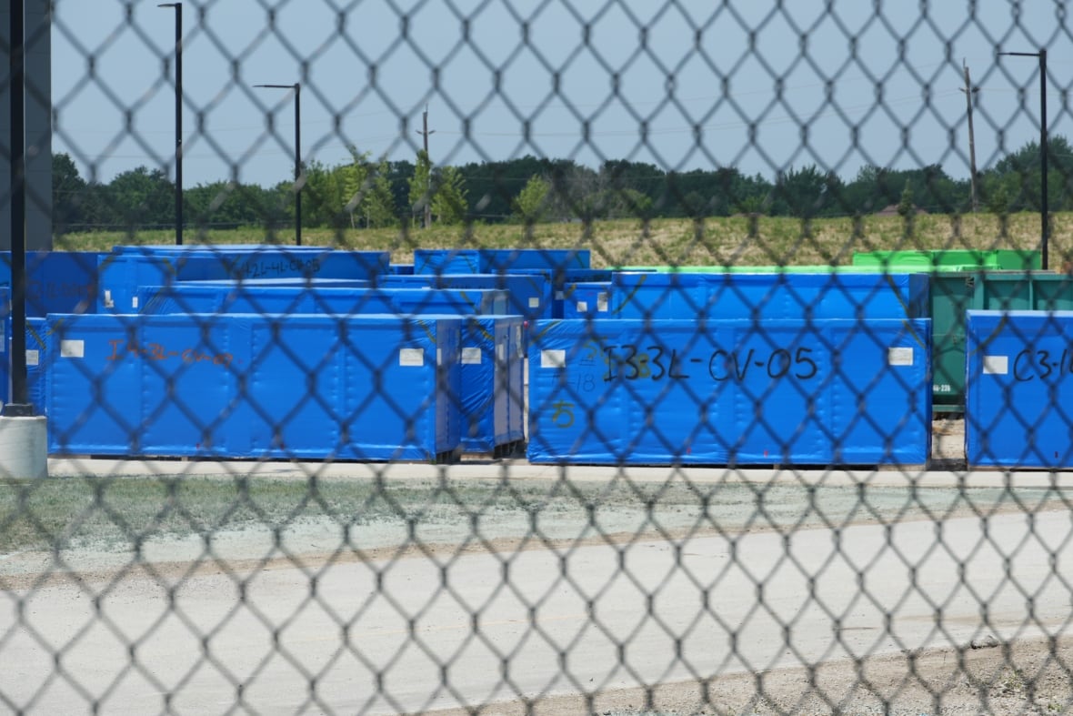 Blue shipping containers are seen behind a fence