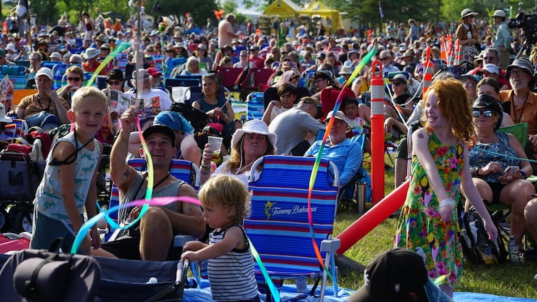 Children play with ribbons while adults sit in seats.