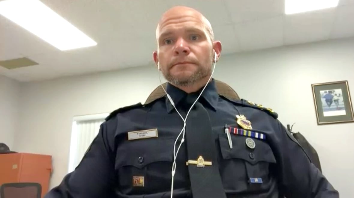 A bald white man in a navy police uniform sits in an office