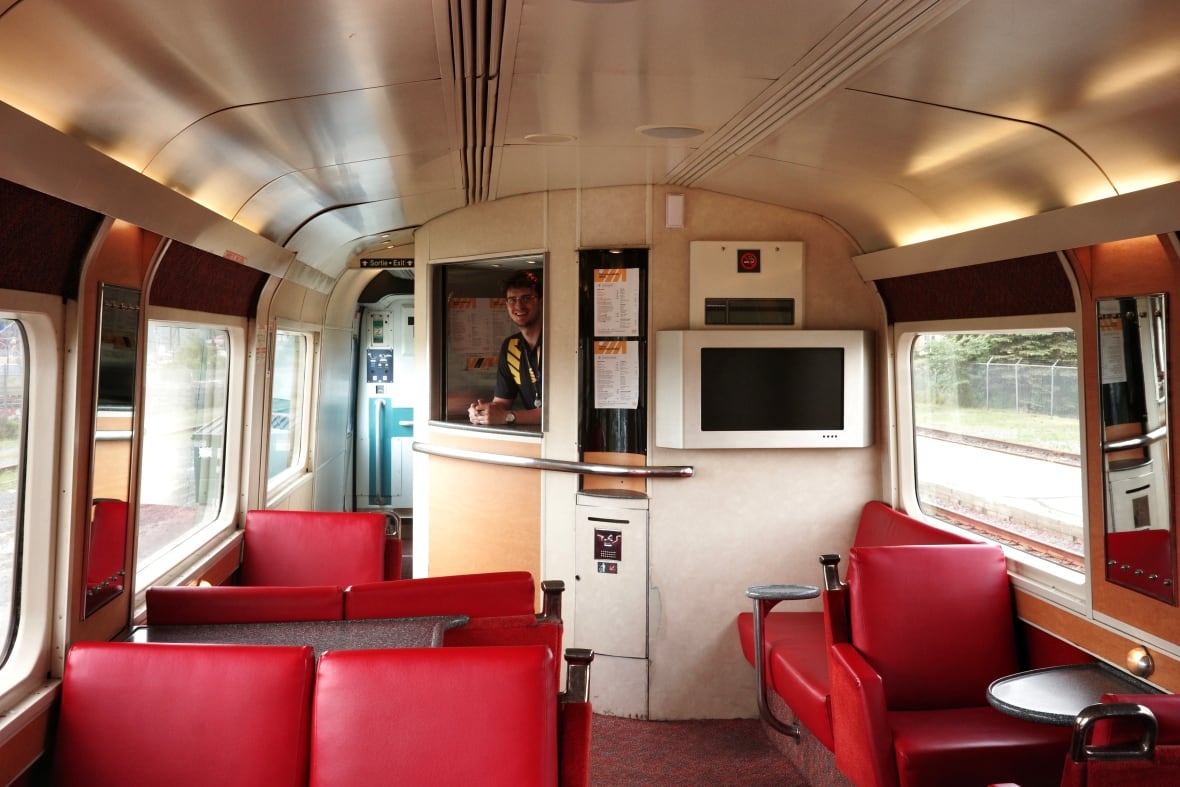 Interior of a train with red seats and an attendant standing at a window