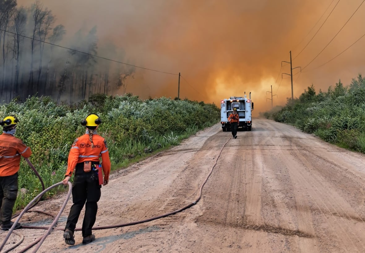 Fire crews are seen on a dirt road beneath smoky orange skies.