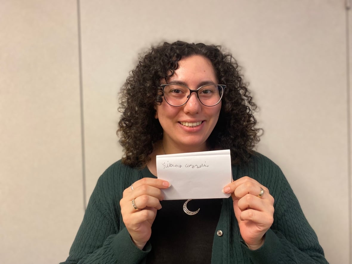 A young woman holds a small piece of paper with her name handwritten in pen.