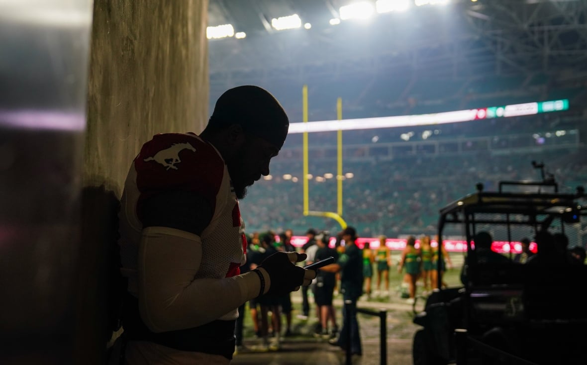 A player from the Calgary Stampeders, wearing a red and white jersey, stands in silhouette outside of a tunnel. A haze of wildfire smoke can be seen in front of the stadium lights.