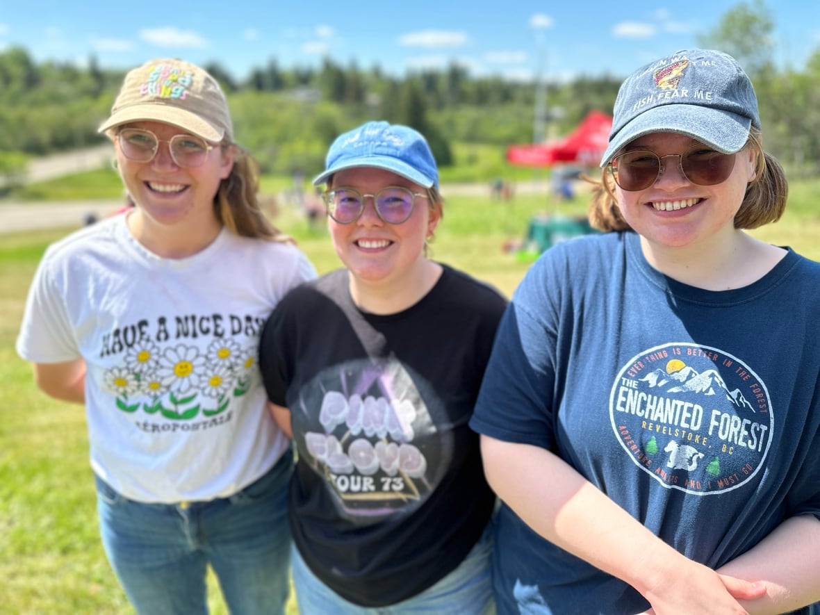 Three young grads pose for a photo wearing baseball caps in a field. 